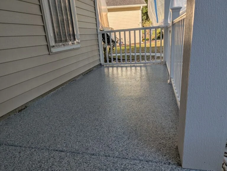 A textured porch floor framed by siding and white railings.